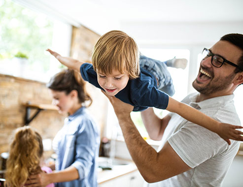 Happy little boy having fun with his father at home. There are people in the background.