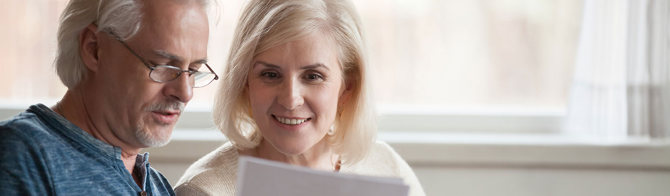 Happy old middle aged couple holding reading good news in document, smiling senior mature family excited by mail letter, checking paying domestic bills online on laptop, discussing budget planning