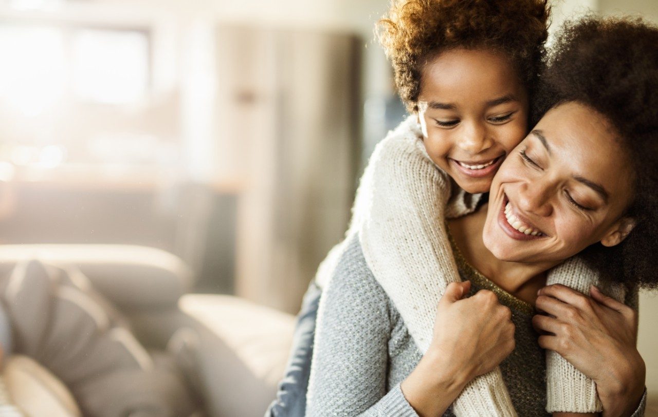 Happy black girl embracing her mother with great affection at home. Copy space.
