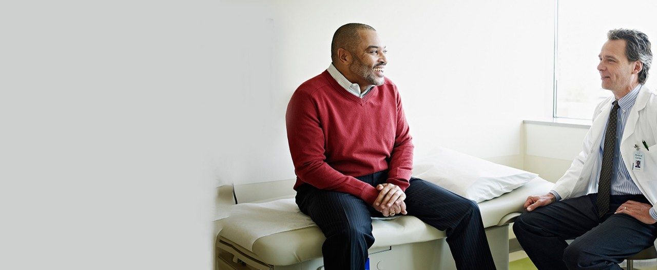 Mature male patient sitting on exam table  in discussion with doctor in exam room