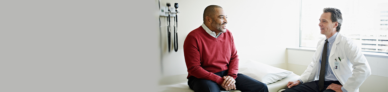 Mature male patient sitting on exam table  in discussion with doctor in exam room