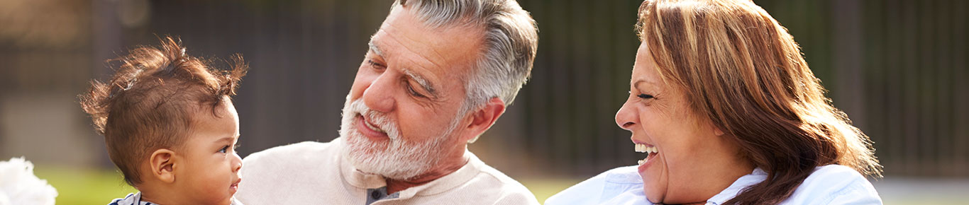 Senior couple sitting in the garden with their baby grandson, smiling at him, front view