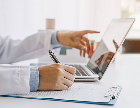 Doctor in hospital writing medical documentation and using laptop