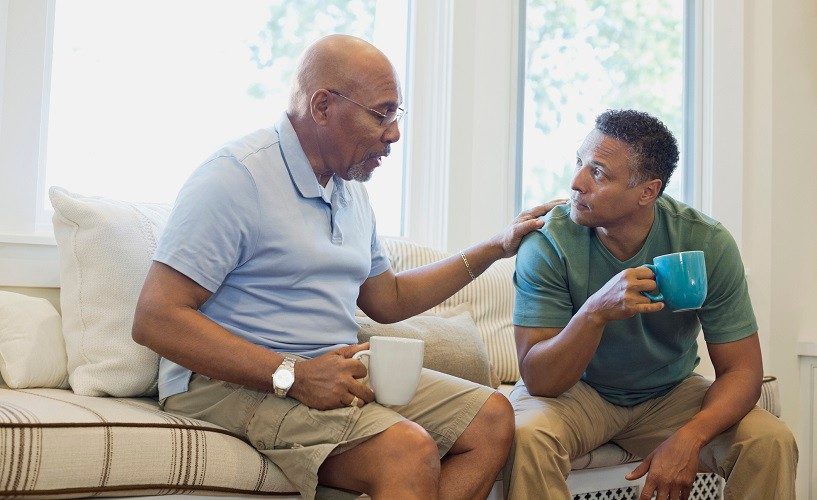 Senior father and son talking while having coffee on sofa.