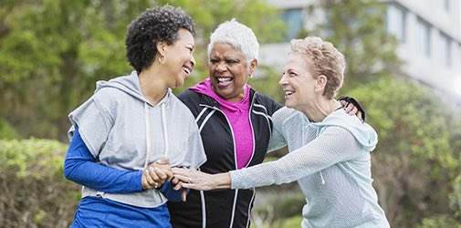 Three multi-ethnic women wearing hooded sweatshirts, hanging out together in the city, talking and laughing while they take a walk. The woman with black hair is in her 50s and her senior friends are in their 60s.